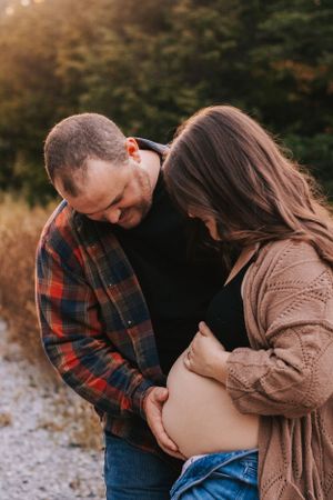 Tender moment between expectant couple during outdoor fall photoshoot.