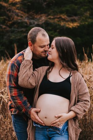 Couple sharing intimate moment during maternity photography session in natural setting.