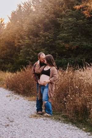 Artistic maternity photos captured on gravel path with autumn foliage in background.