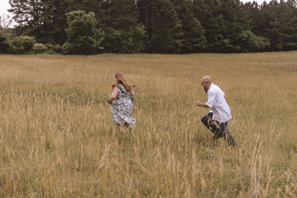 Engaged couple playfully running in the grass at Anne Springs Greenway in Charlotte, North Carolina