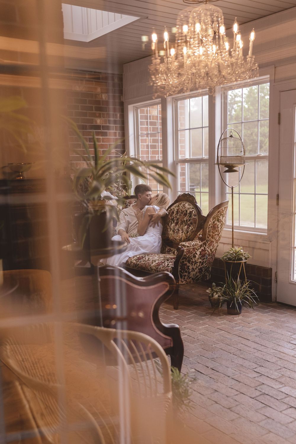 Creative portrait through the glass door of a engaged couple on a couch at Willow and Stone Events in Mocksville, North Carolina