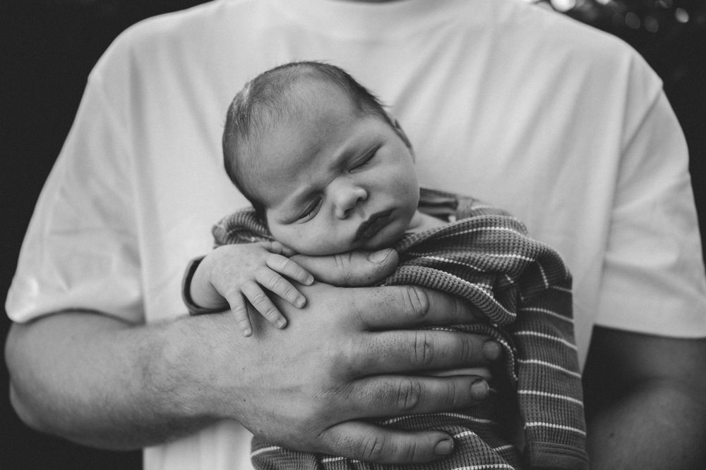 Black and white photo of a newborn baby sleeping peacefully in a father's hands against his chest.