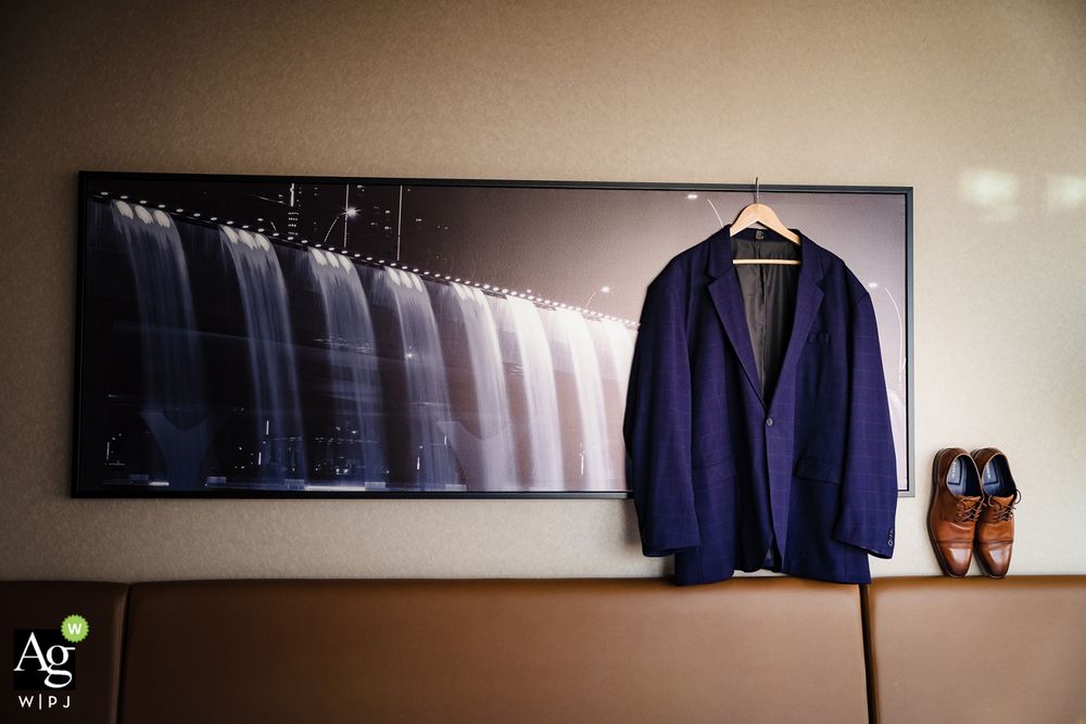 A navy blue suit jacket hangs next to framed artwork showing a gradient of suit jackets, with brown dress shoes on display.