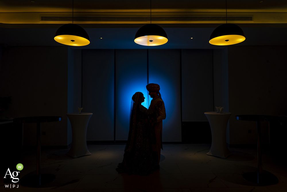 A romantic silhouette of a couple against a blue backlit wall with three golden pendant lights above them.