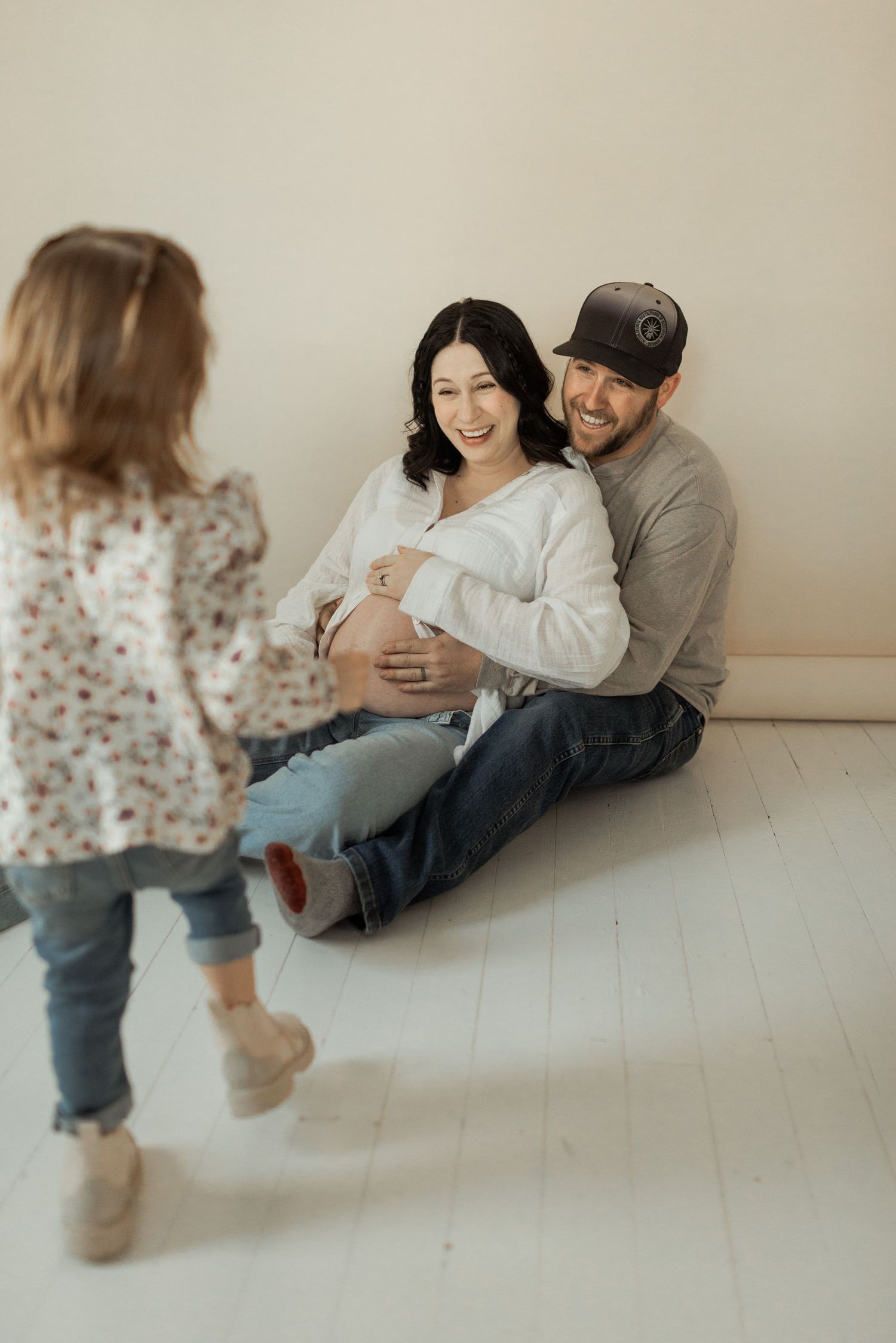 Family sits together on a white floor during an intimate maternity photo session.