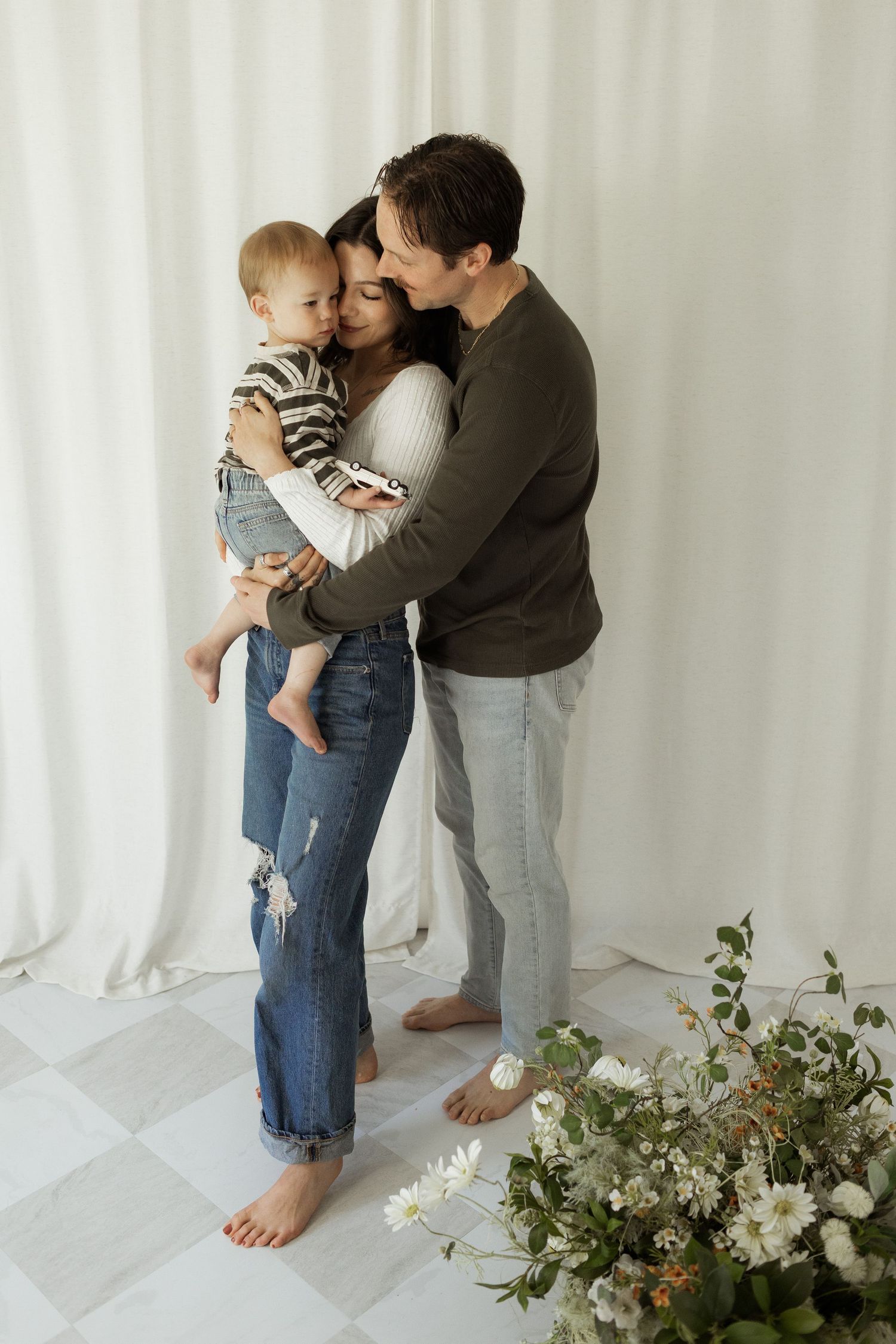 Family sits together on a white floor during an intimate maternity photo session.