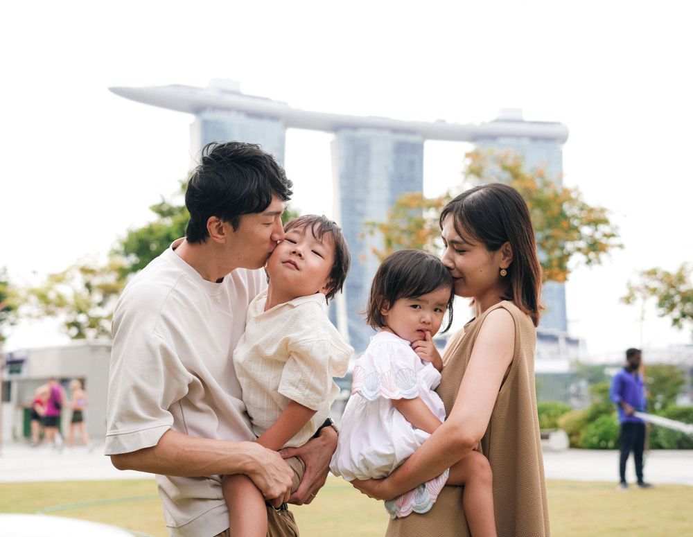 Family laughing and playing together outdoors with iconic Singapore skyline in background.
