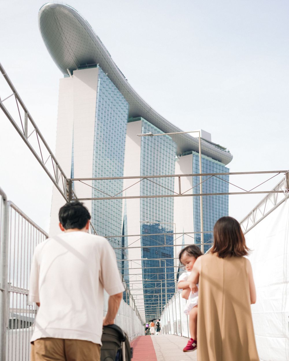A family walks along a bridge with the iconic Marina Bay Sands hotel in Singapore visible behind them.