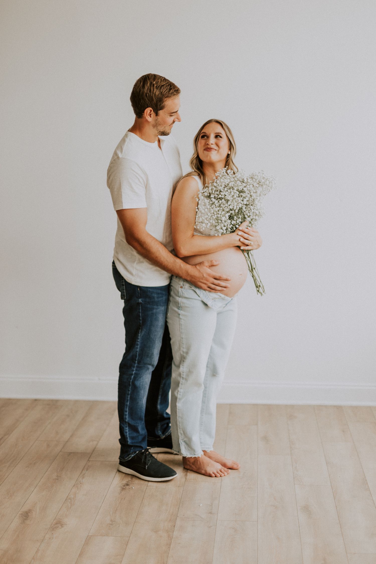 Intimate maternity photo showing couple standing together holding baby's breath flowers.