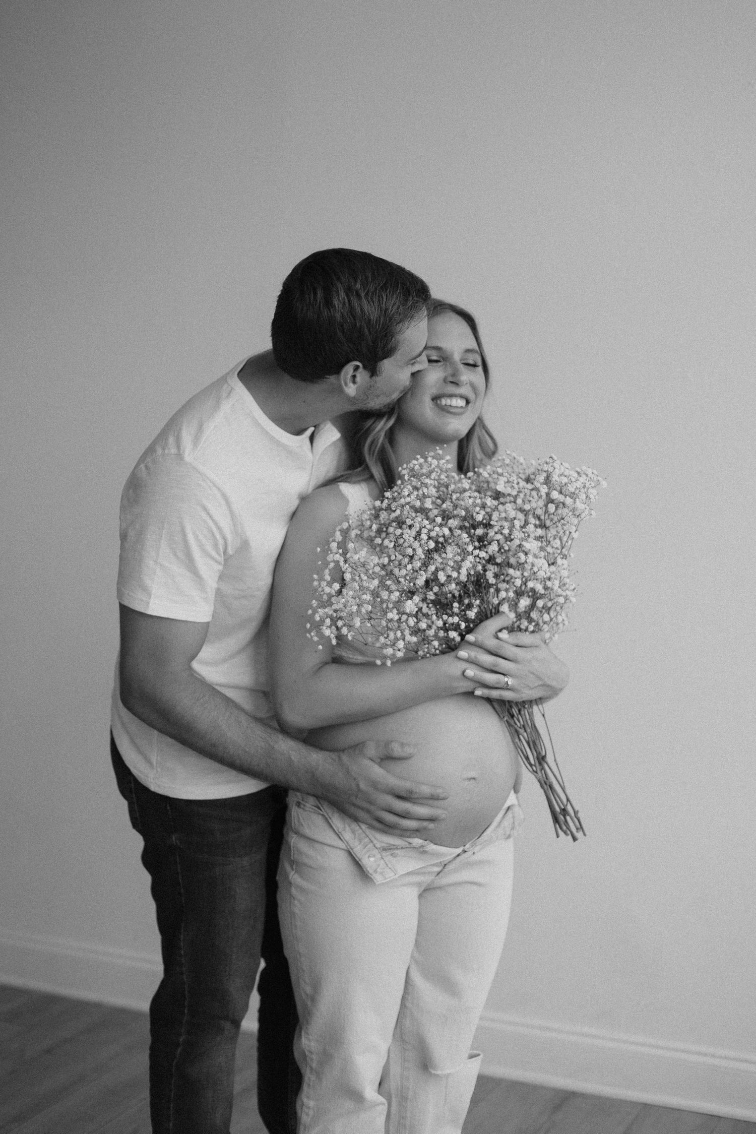 Black and white maternity photo with couple embracing and holding baby's breath flowers.