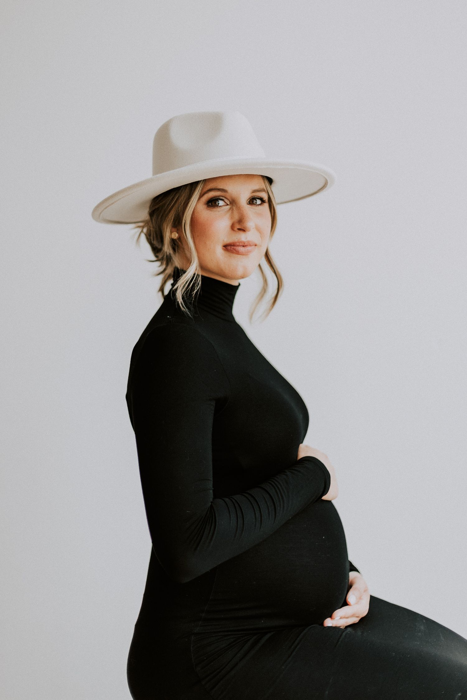 Stylish maternity portrait featuring person in black turtleneck and wide-brim hat.