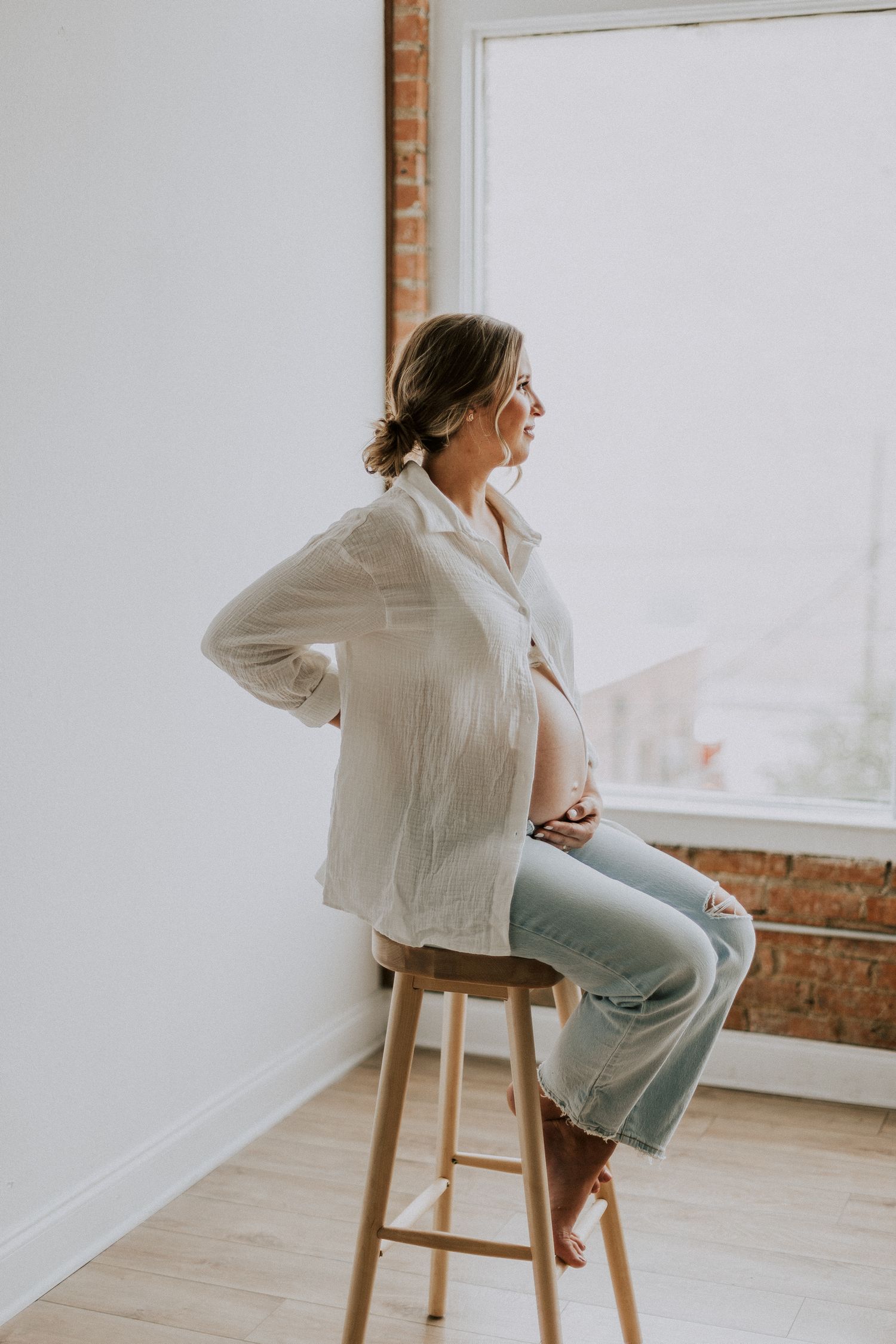 Side view of person sitting on wooden stool during casual maternity photoshoot.