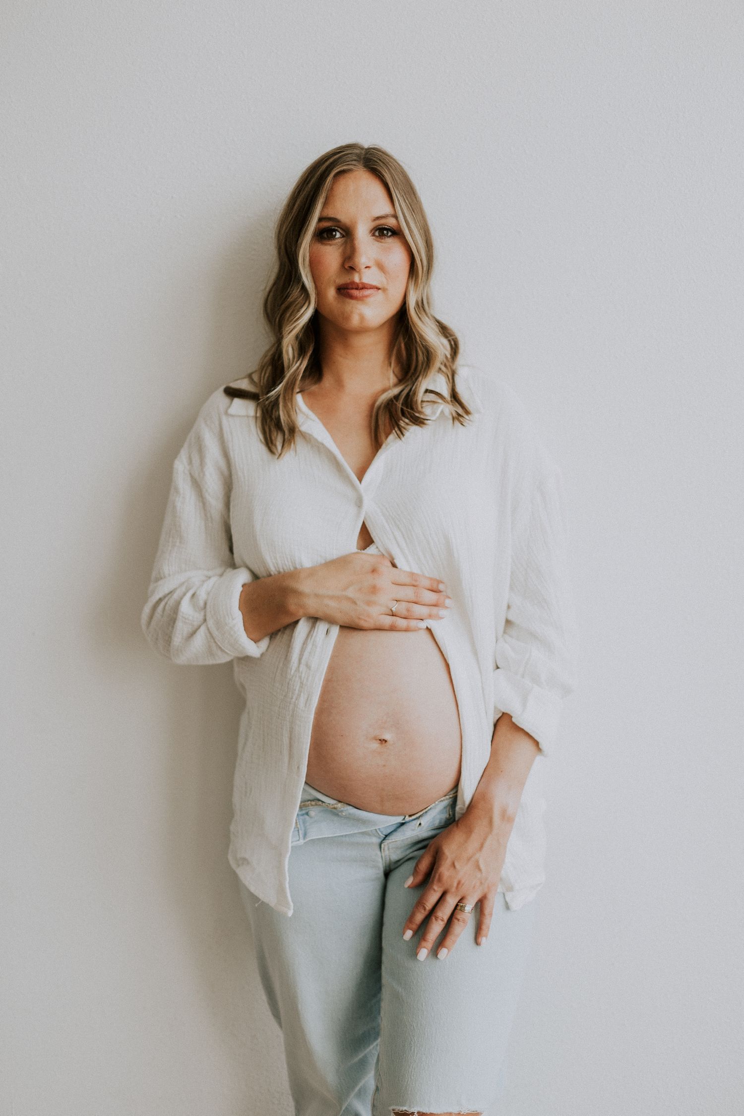 Casual maternity portrait with white button-down shirt and light wash denim.