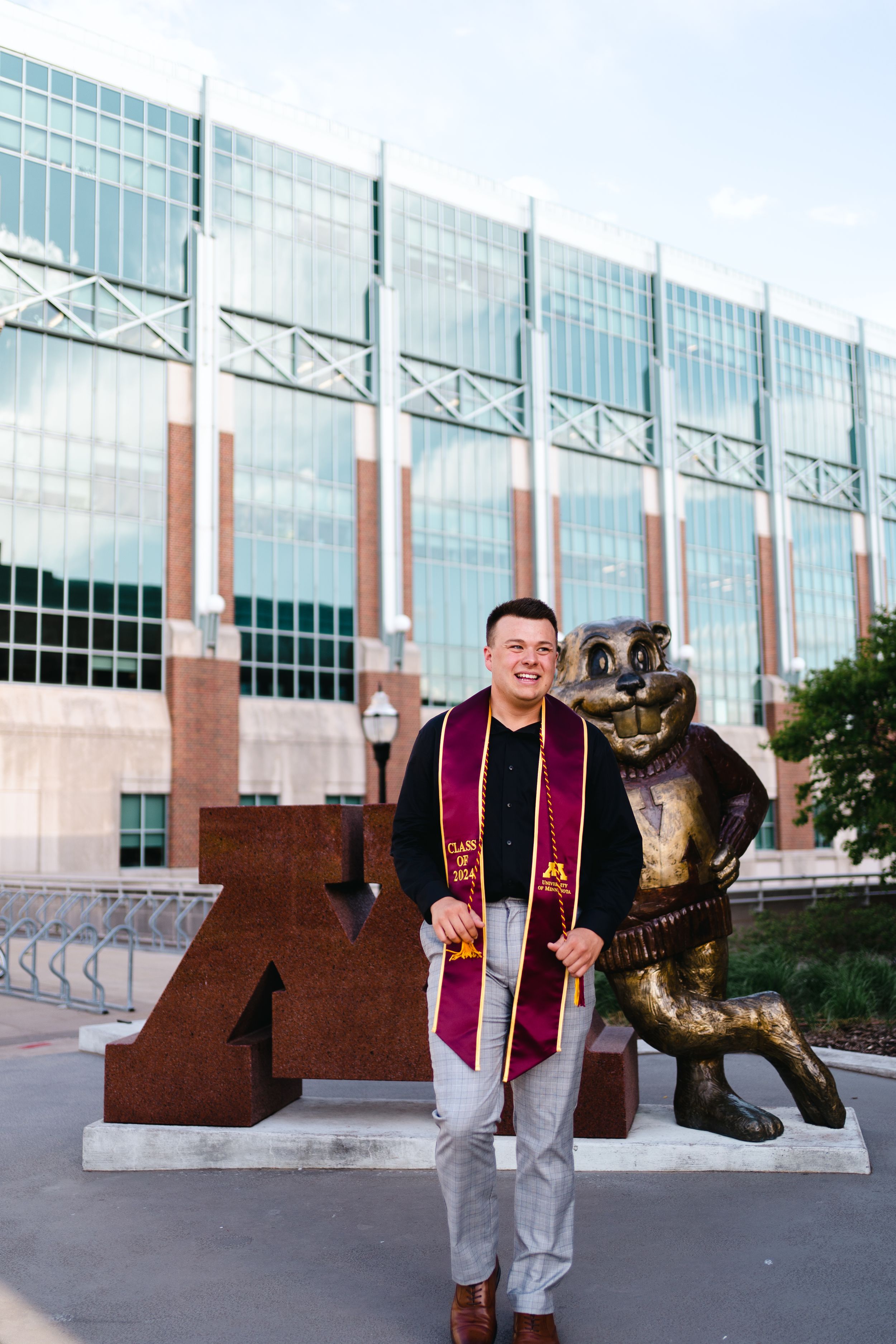 Graduate poses with university mascot statue wearing graduation stole.