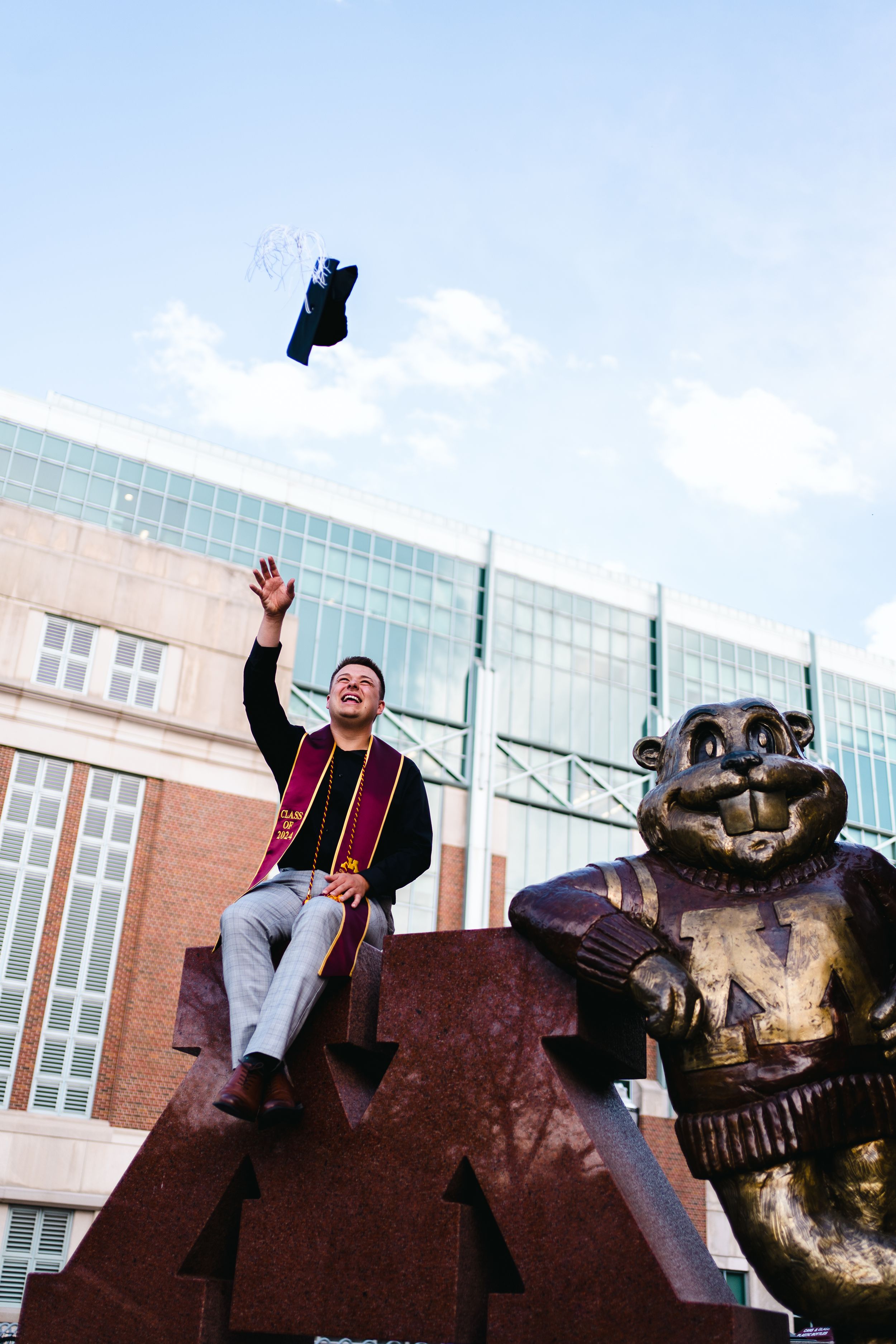 Graduate tosses cap in celebration next to university mascot statue.