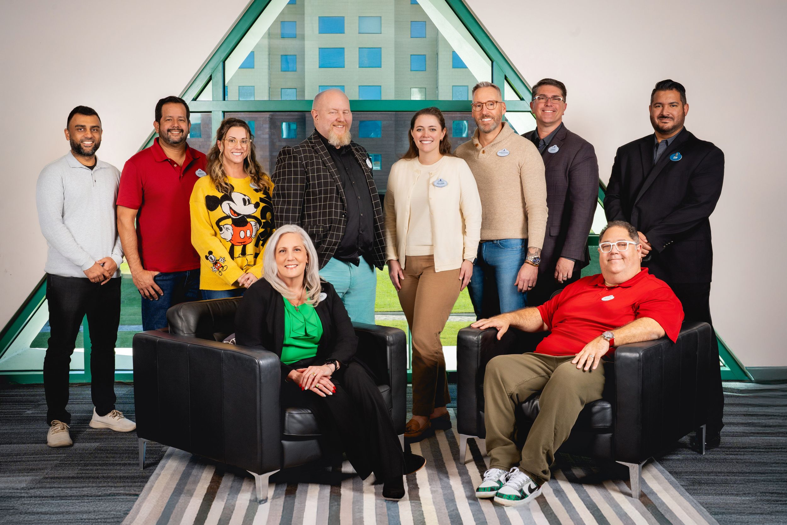 A group photo of team members sitting and standing in front of a turquoise geometric wall in an office setting.
