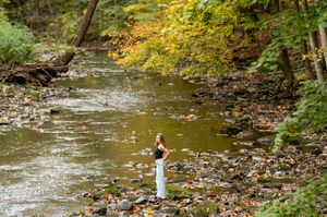 Young woman standing on rocky creek bank surrounded by colorful autumn trees in a forest.