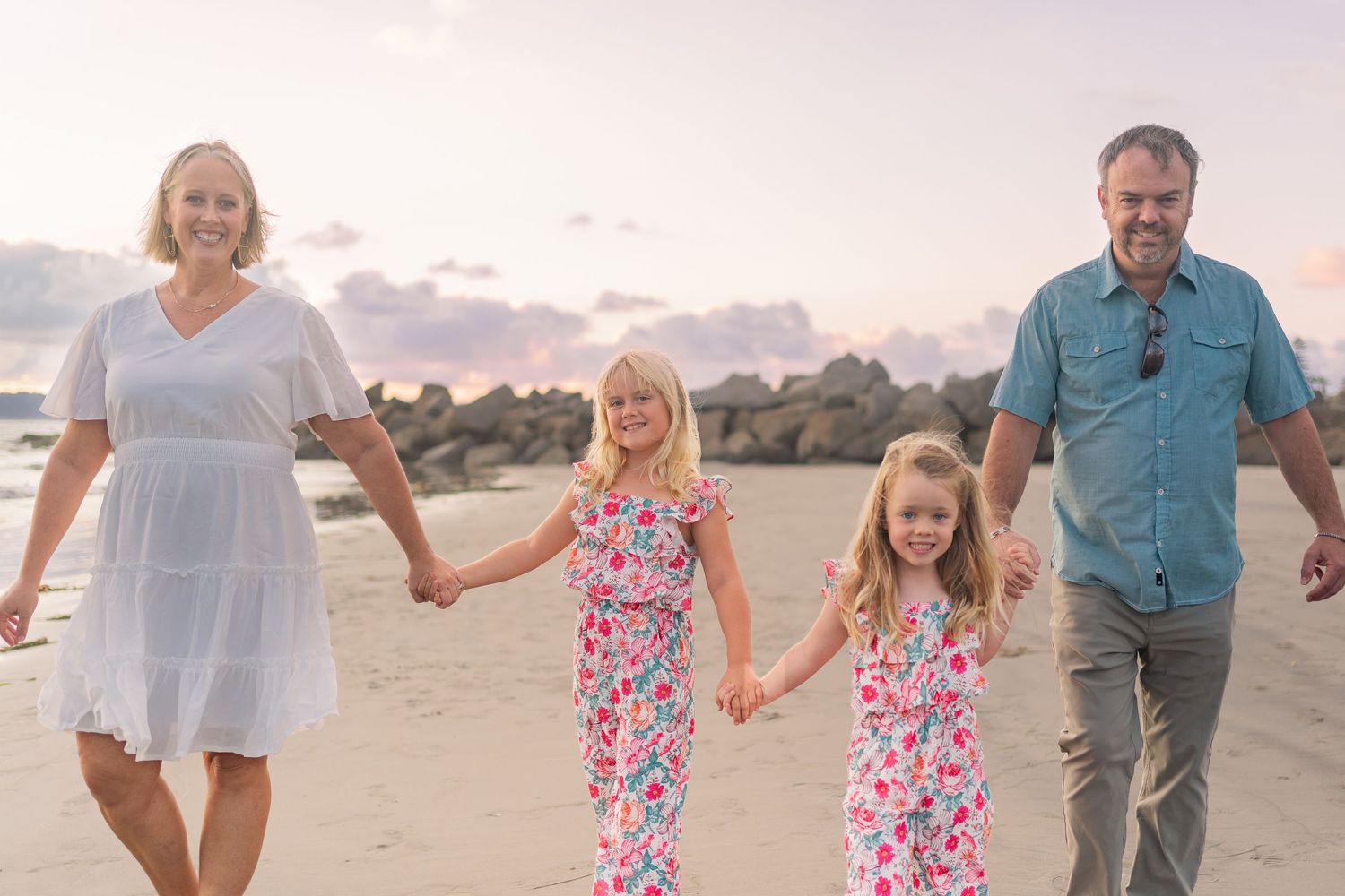 Family holding hands while walking on beach during sunset with ocean in background.