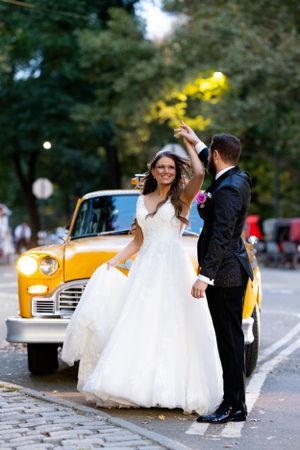 A romantic dance pose next to a yellow taxi cab on a cobblestone street.