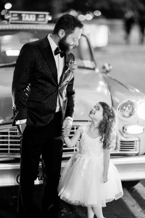 A black and white photo of a formal evening scene with a vintage taxi and formalwear.