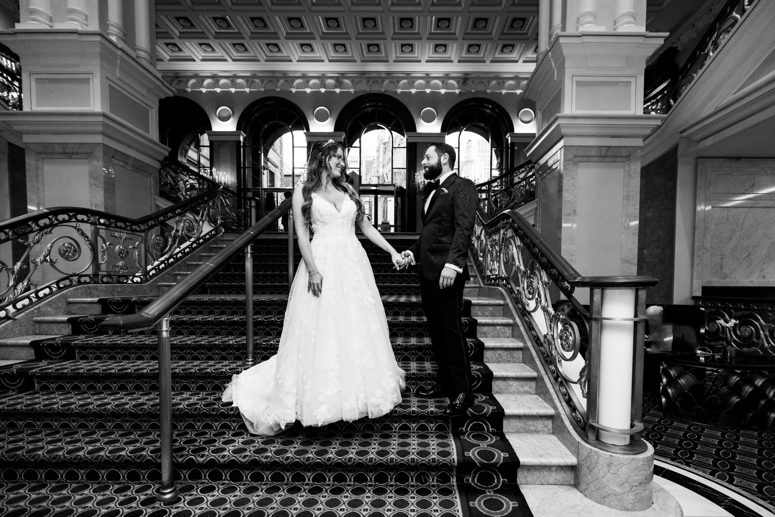 Elegant wedding couple poses on grand staircase of The Lotte New York Palace with ornate architectural details.