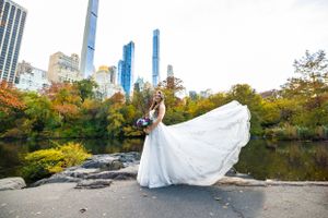An elegant wedding dress billows in the wind against the backdrop of Central Park and NYC skyscrapers.