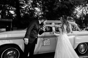 A playful black and white wedding photo featuring a vintage taxi cab.