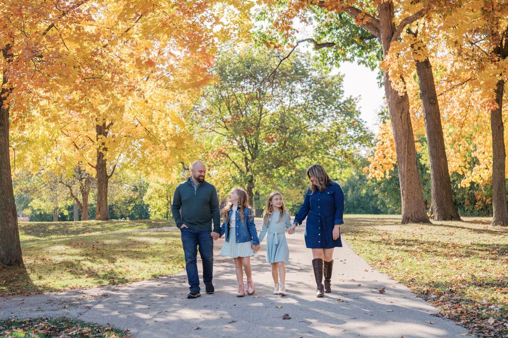 A family strolls along a tree-lined path with beautiful fall foliage overhead.