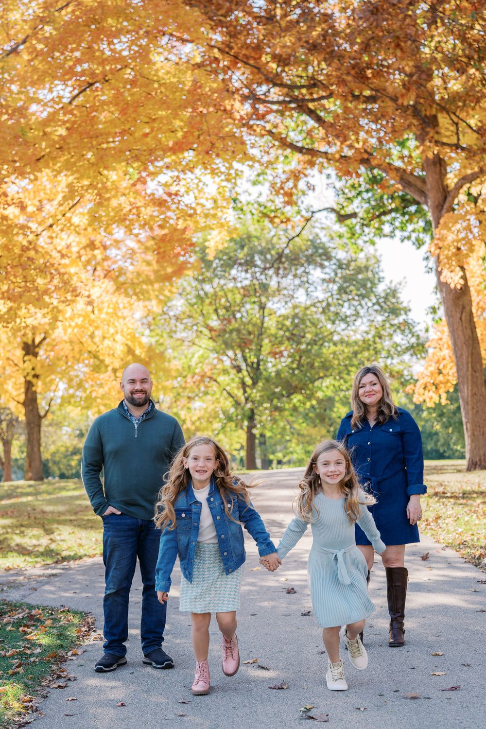 A family walks together on a path surrounded by golden autumn trees during a fall photo session.