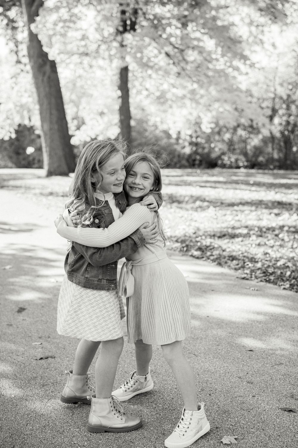 Two children share a sweet hug on a path during a black and white autumn photo shoot.