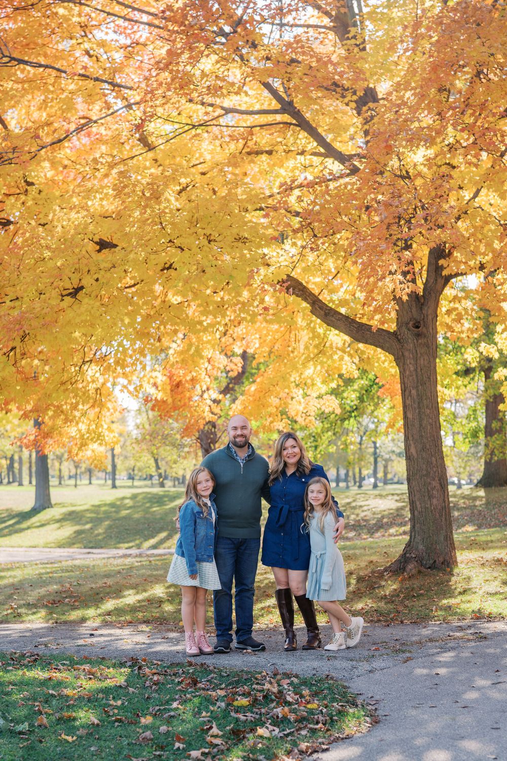 Family standing together under bright yellow fall foliage on park path.