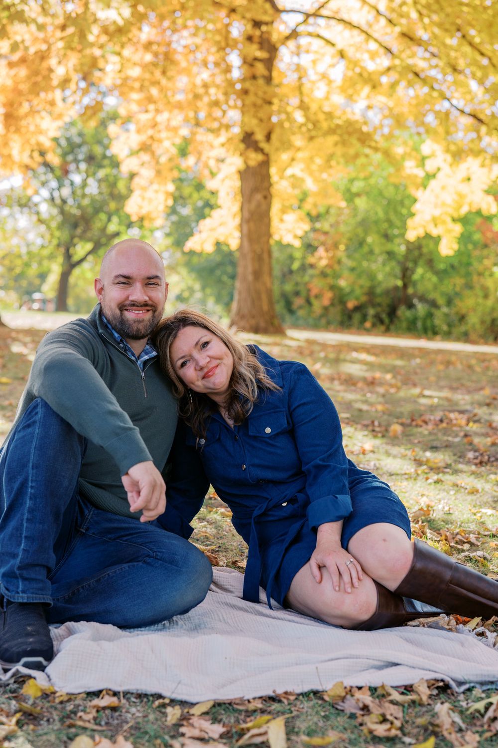 A couple shares playful moments on a blanket surrounded by fall leaves.