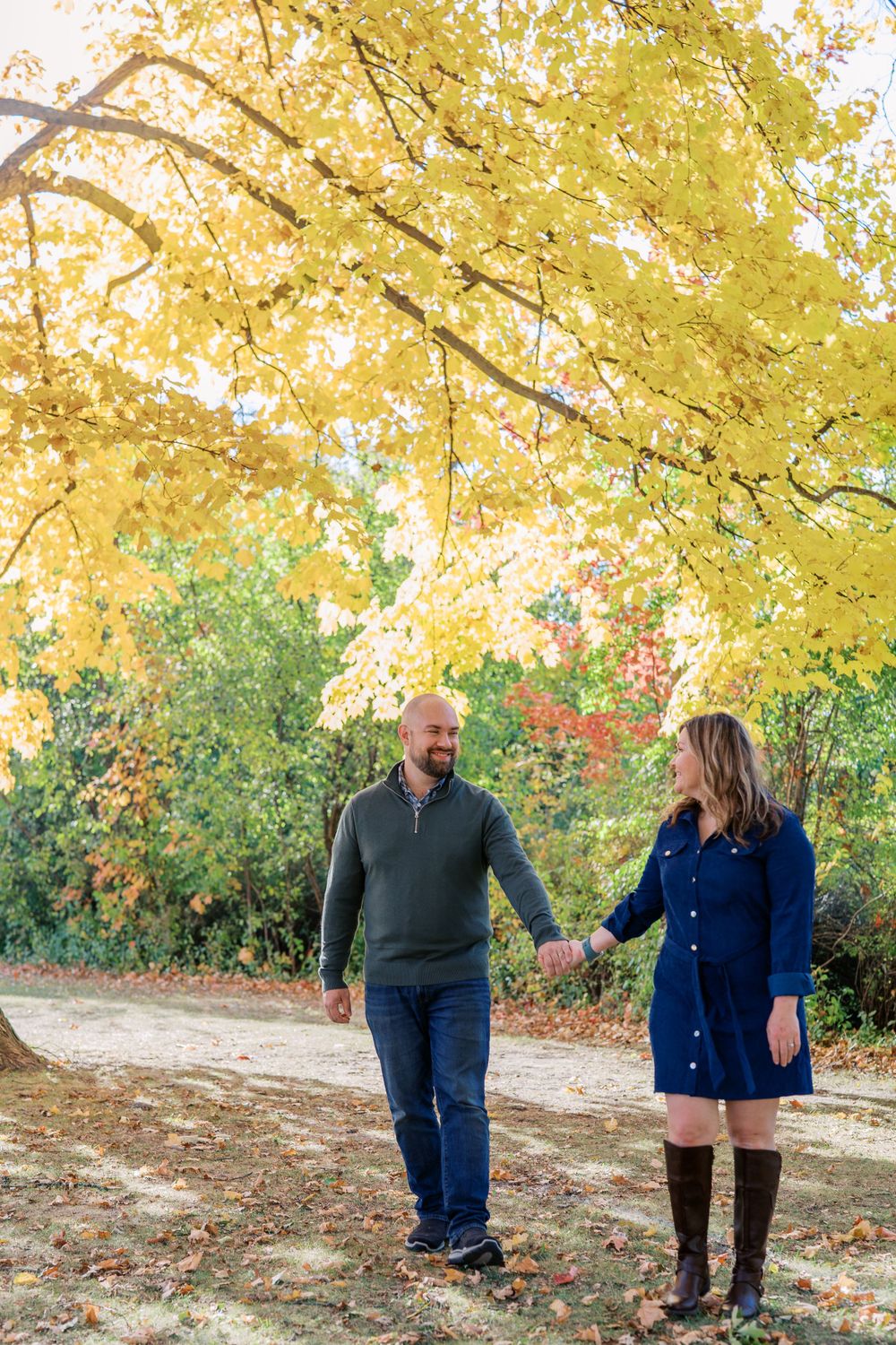 Couple walking and laughing together beneath yellow fall foliage on a nature path.