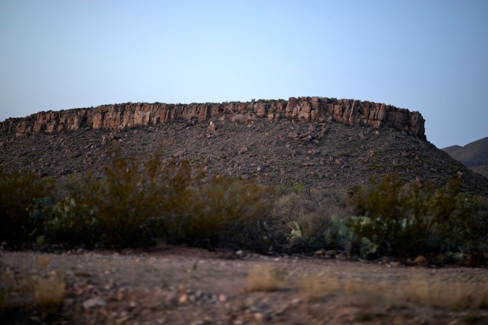 A rugged desert mesa with steep cliffs rises against a dusky sky in the American Southwest.