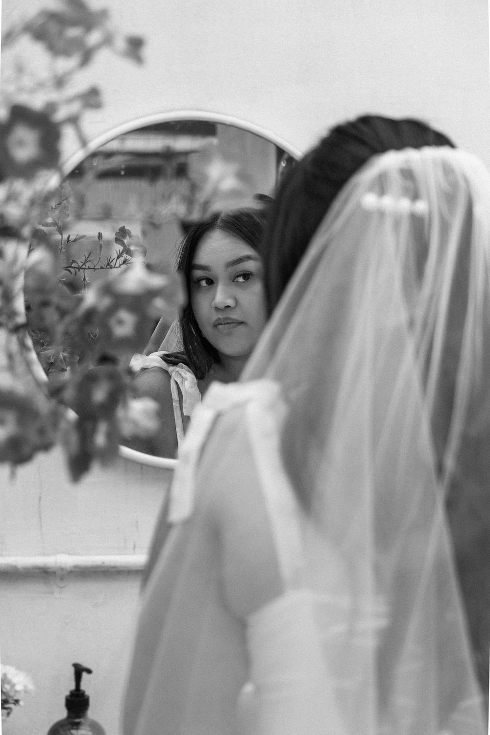 Black and white photo showing a candid getting-ready moment with a delicate bridal veil in soft natural light.