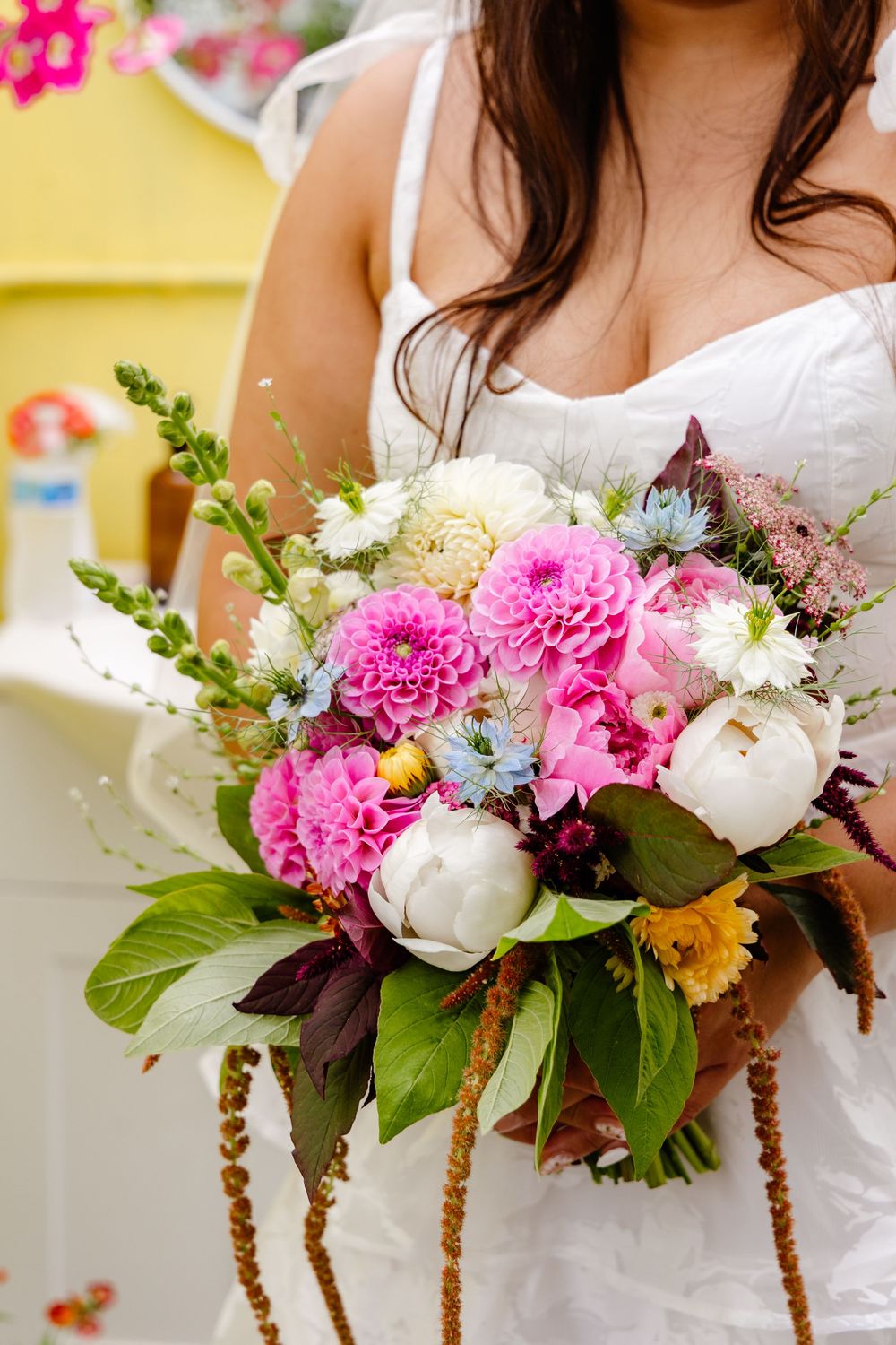 Row of bridesmaids holding colorful bouquets with pink carnations, white peonies and blue accents for a summer wedding.
