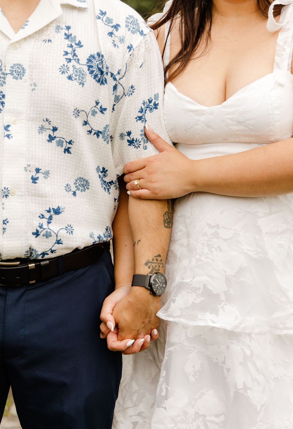 Close up of couple holding hands with floral button up shirt and white wedding dress showing tattoos and details.