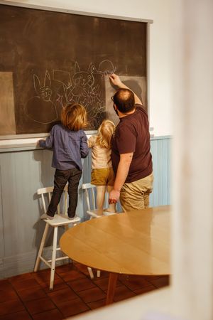 Papa et ses enfants dessinant ensemble sur un tableau de craie, scène du quotidien pleine de tendresse à Saint-Étienne