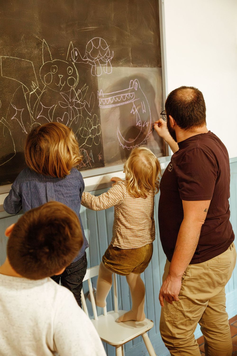 Photographie d'un père et ses enfants devant un tableau en train de dessiner à la craie pendant une séance photo famille à domicile Loire