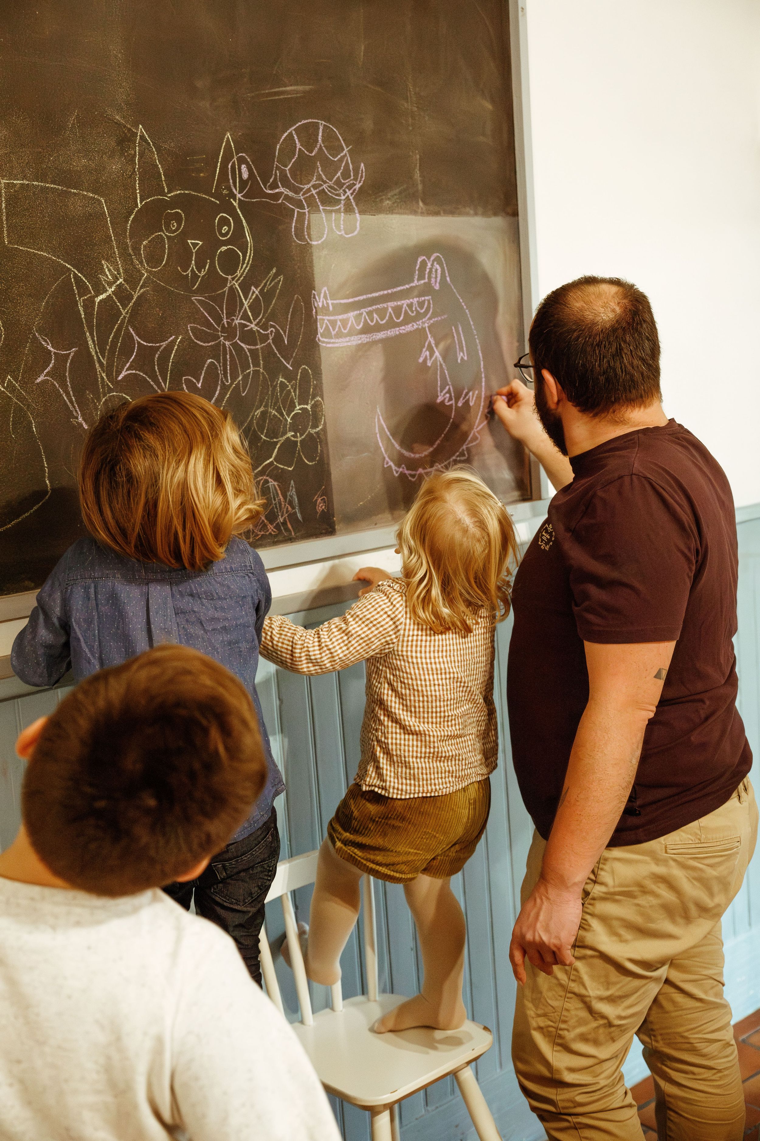Photographie d'un père et ses enfants devant un tableau en train de dessiner à la craie pendant une séance photo famille à domicile Loire