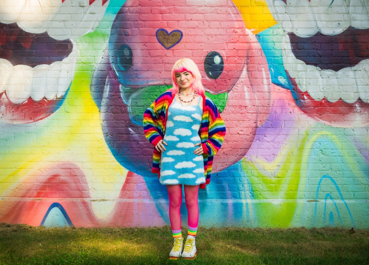 A person stands against a vibrant street art mural with colorful swirls, hearts and smiling faces in bright neon colors.