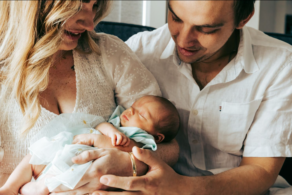 Tender newborn baby swaddled in light blue being held by parents.