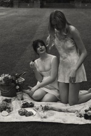 A vintage-style black and white photo of two friends enjoying a garden picnic.