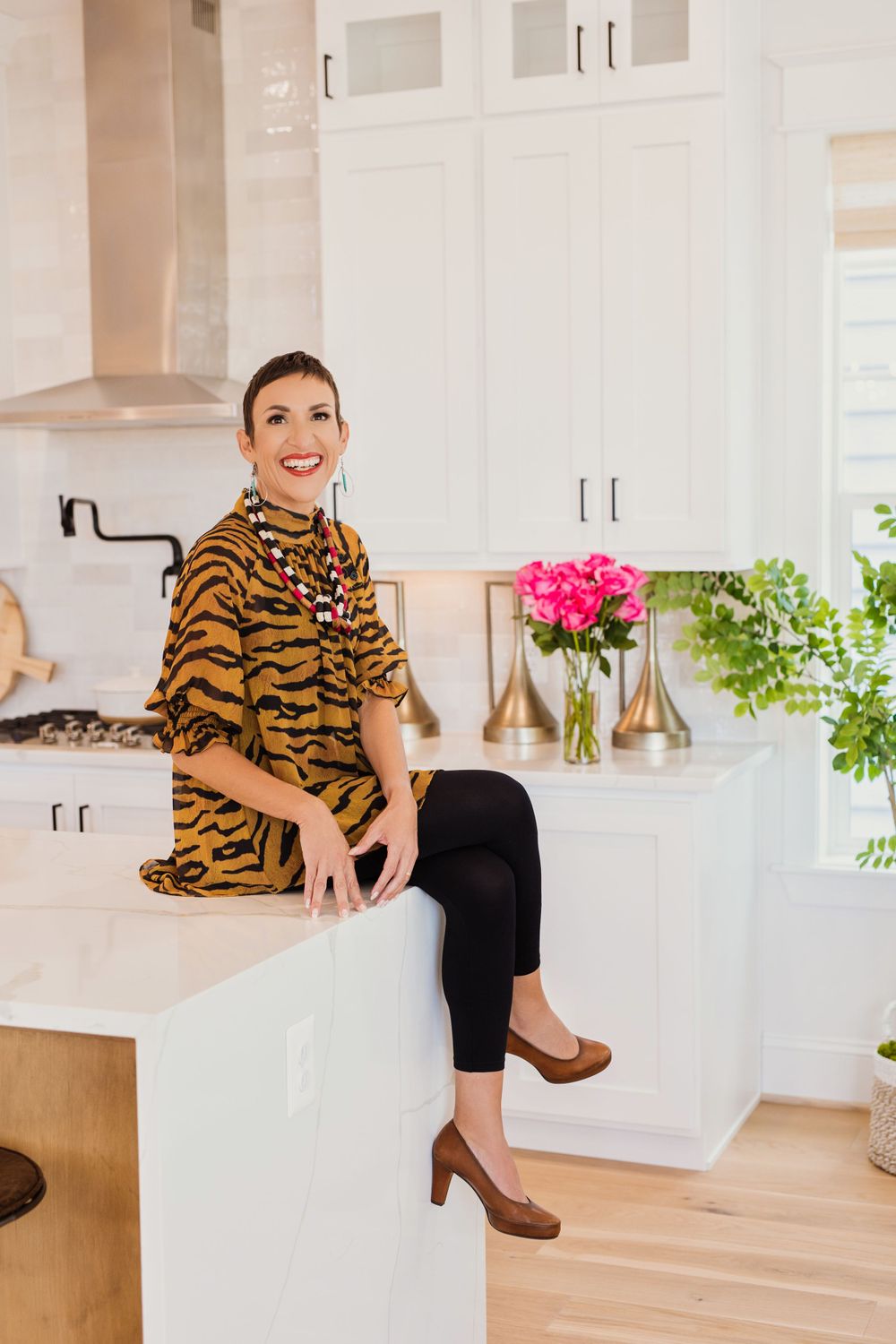 Modern white kitchen interior with tiger print blouse, pink flowers in a vase, and houseplants on counter.