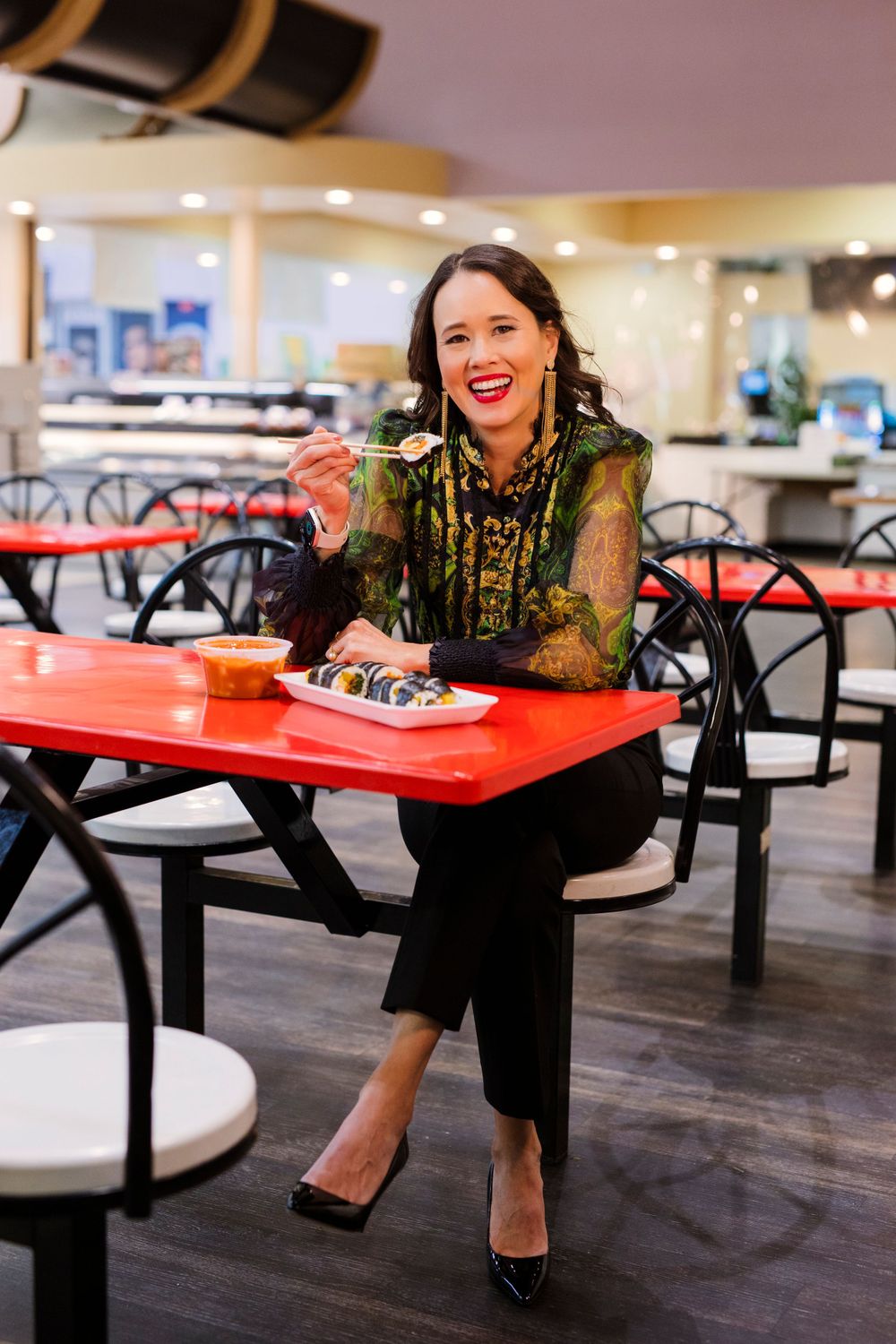 Someone in a green sequined top dines at a casual restaurant with red tables and black chairs.