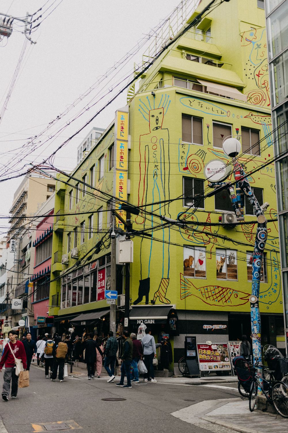 Yellow building with street art and murals in an urban Japanese shopping district.