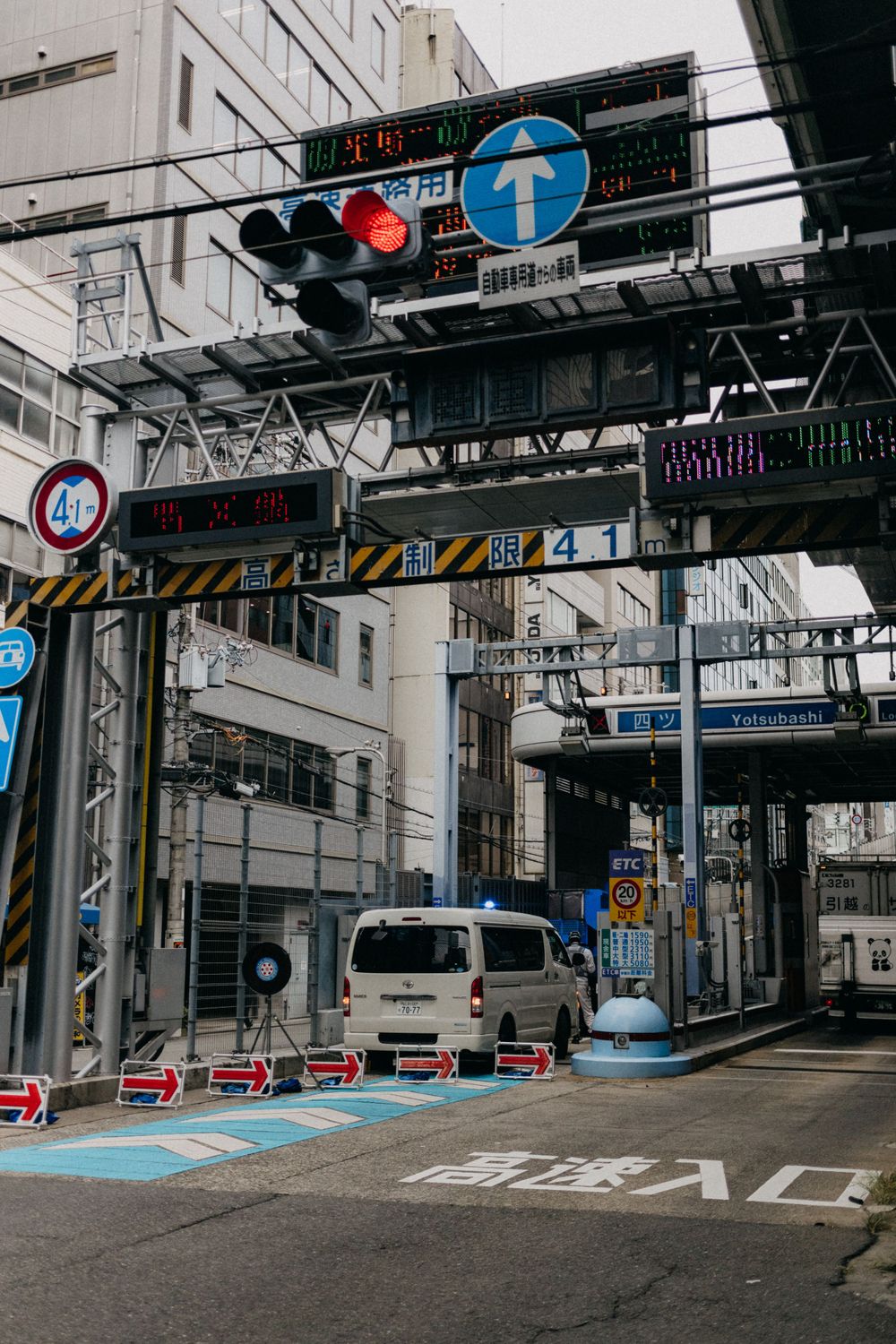Urban street in Japan with traffic signals and blue directional signs mounted on an overhead structure.