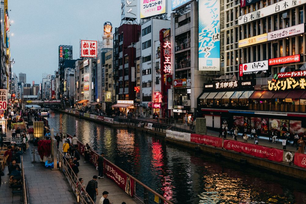 Dotonbori canal in Osaka at dusk with neon signs reflecting on the water.