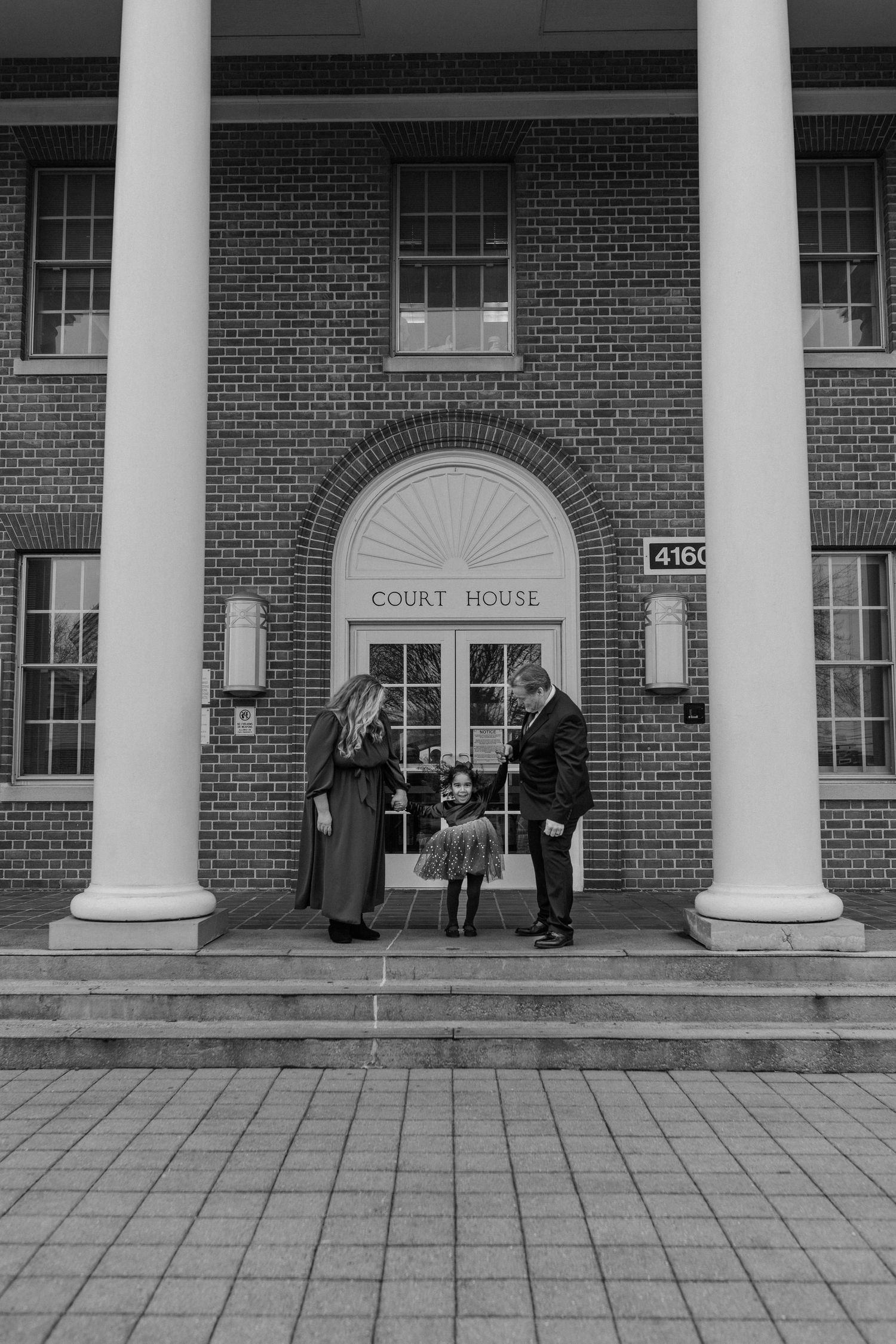 Black and white photo of three people standing at courthouse entrance with white columns and brick facade.