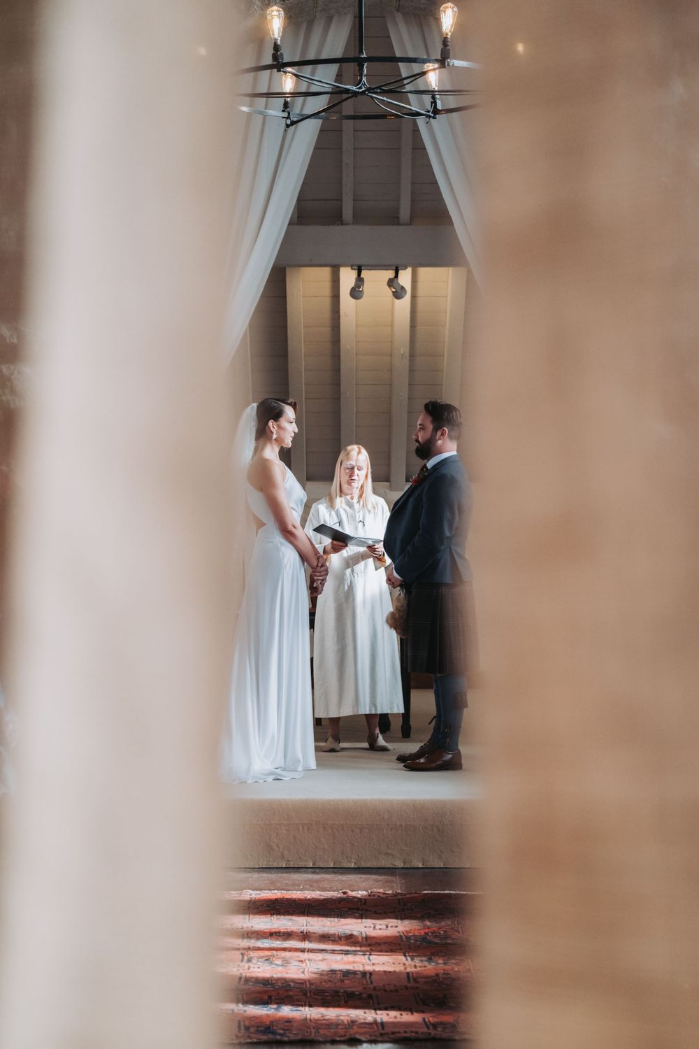 Bride and groom exchange vows with officiant in elegant indoor wedding ceremony.